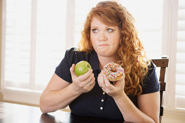 Image of women holding an apple in one hand and a donut in the other.