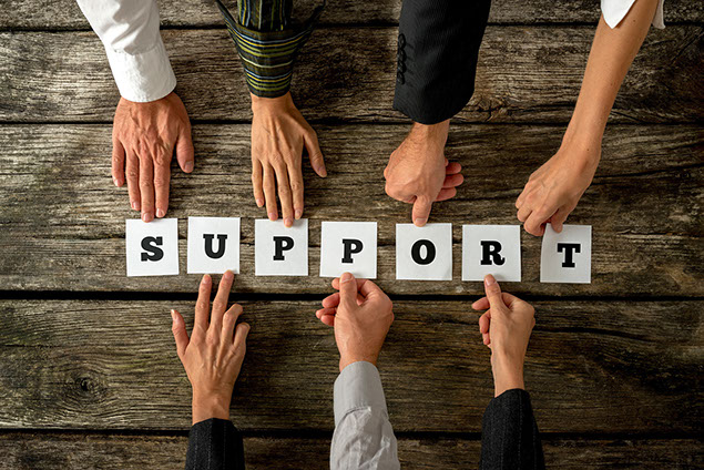 Seven people holding white cards with letters to assemble the word SUPPORT.