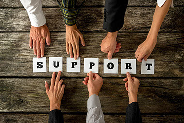 Seven people holding white cards with letters to assemble the word SUPPORT.