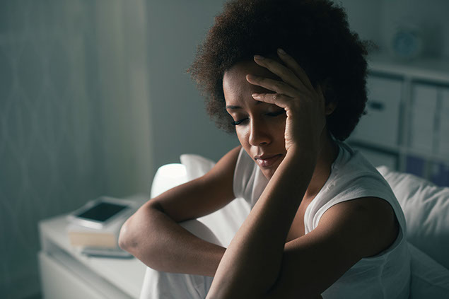 Image of women sitting in bed and touching her forhead.